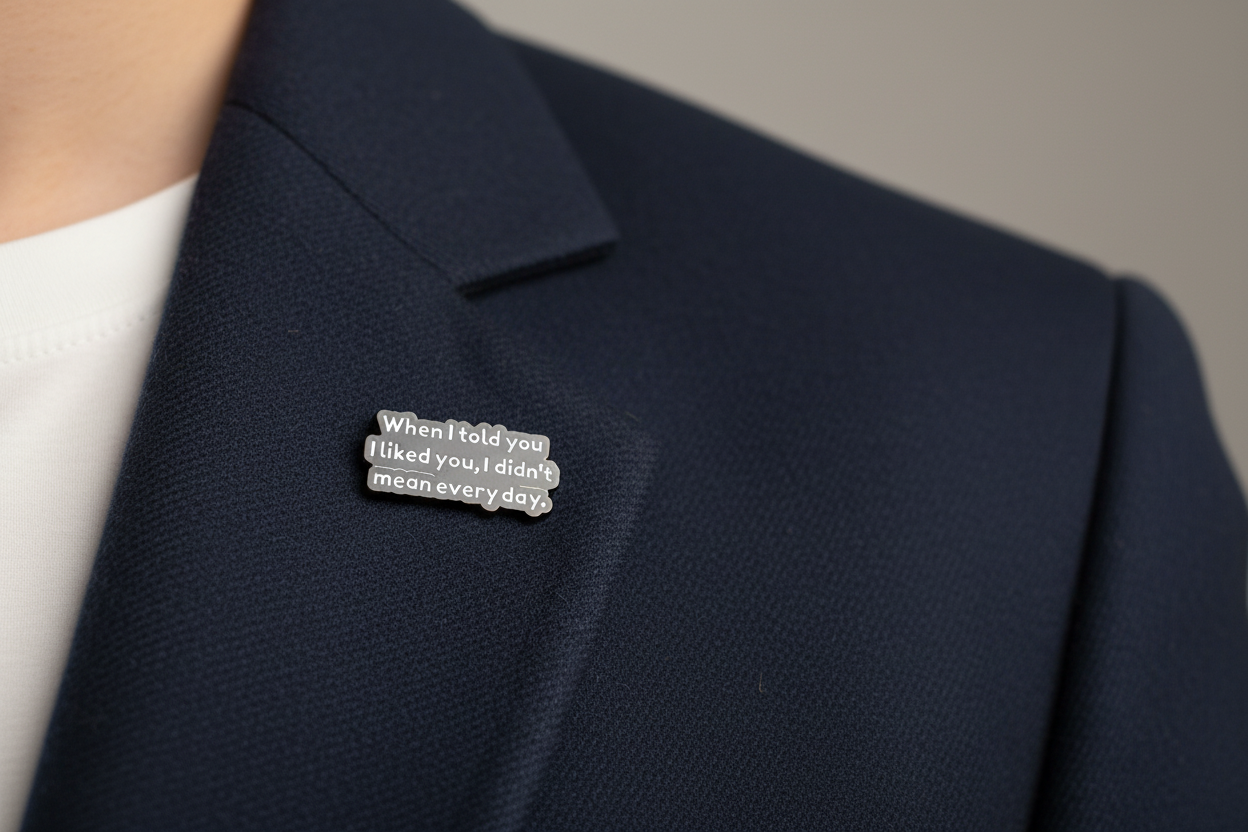 black enamel pin with white text and a sarcastic saying on a navy fabric background