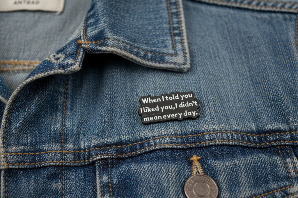 black enamel pin with white text and a sarcastic saying on a denim background