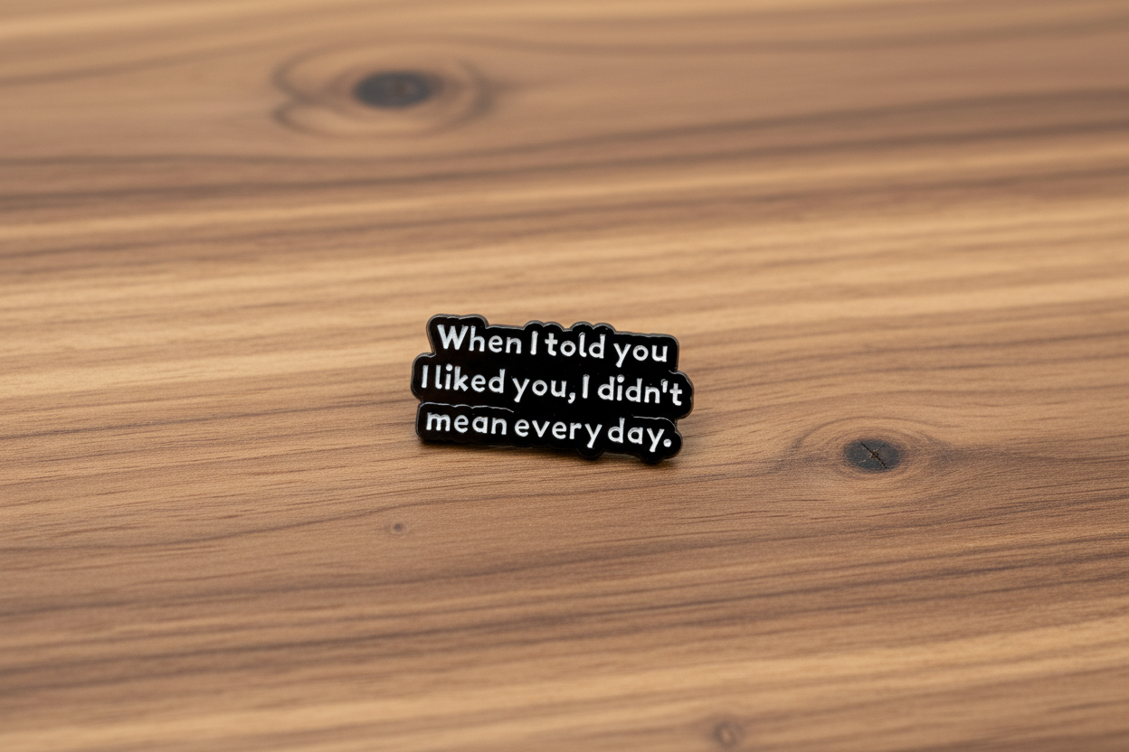 black enamel pin with white text and a sarcastic saying on a wood background