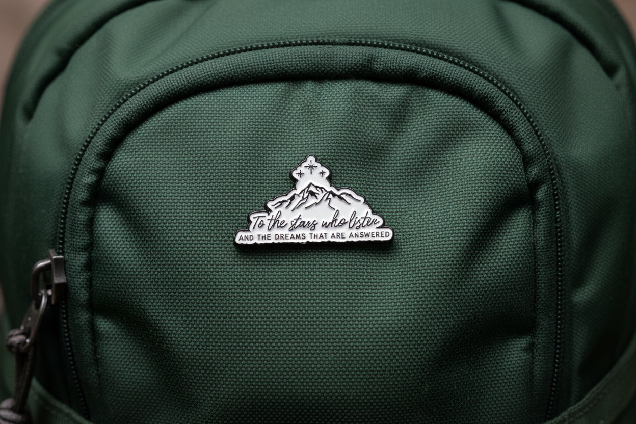 white and black enamel pin with text on a green book bag