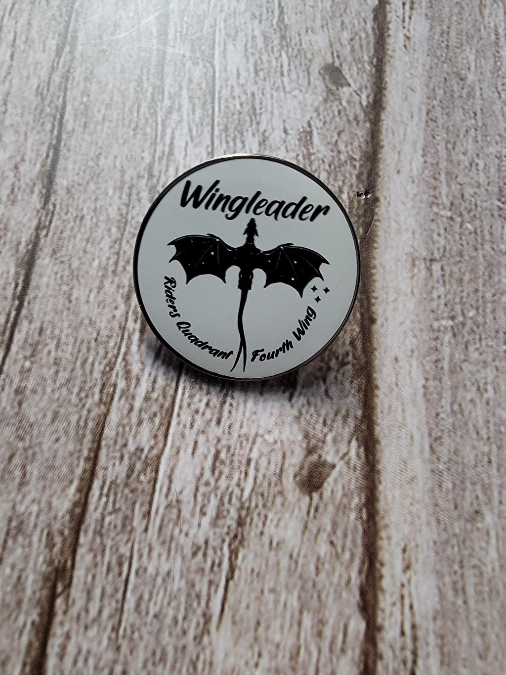 Round badge with 'Wingleader' text and bat design on a wooden surface